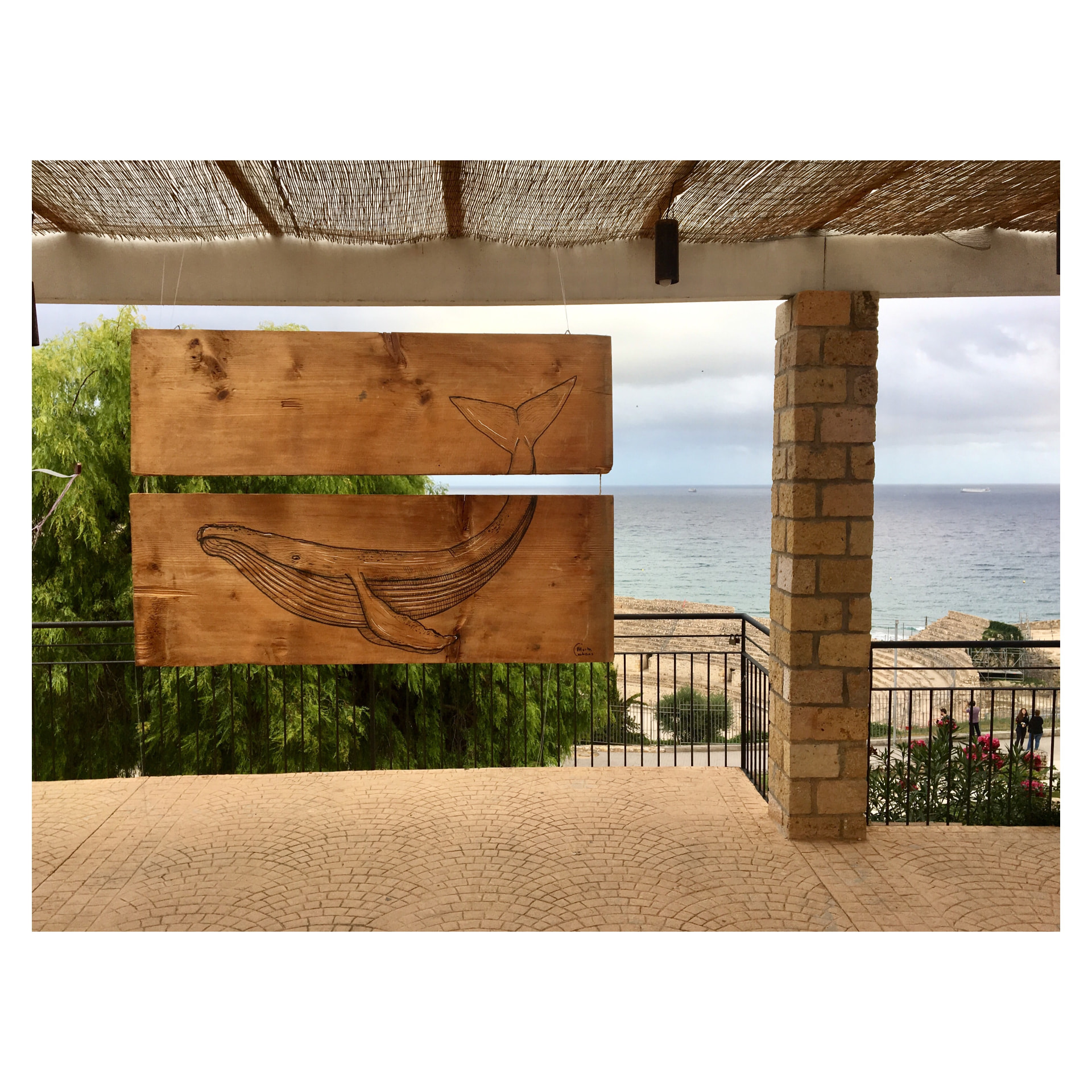 Balena dibuixada sobre fustes penjades davant del mar de Tarragona